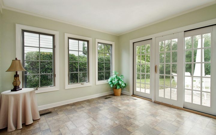 A bright sunroom featuring large French doors and windows with a view of the garden, furnished with a table lamp on a draped round table and a potted plant.