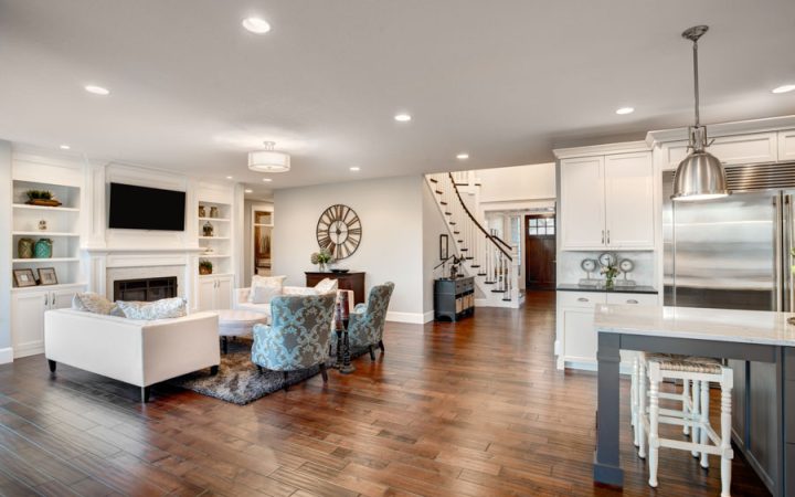 An expansive open concept living space with a white built-in media center, dark hardwood floors, and a connected kitchen area, elegantly designed for seamless living and entertaining.