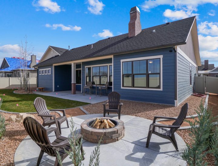 A contemporary backyard patio featuring a circular firepit with surrounding Adirondack chairs, complemented by a neatly maintained lawn and concrete paths.